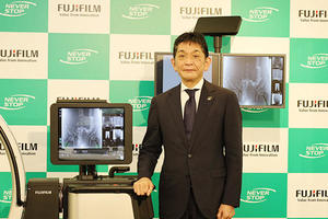 FUJIFILM DR CALNEO CROSSの前に立つ秋山雅孝 氏（メディカルシステム事業部長）